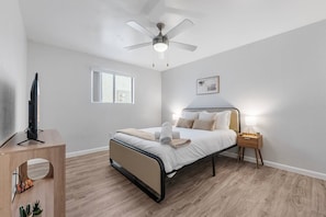 A bedroom with a bed, bedside lamp, ceiling fan, and a television on a stand. - Comfortable Mesa Retreat, 2 Queen Beds, & Pool (Mesa)