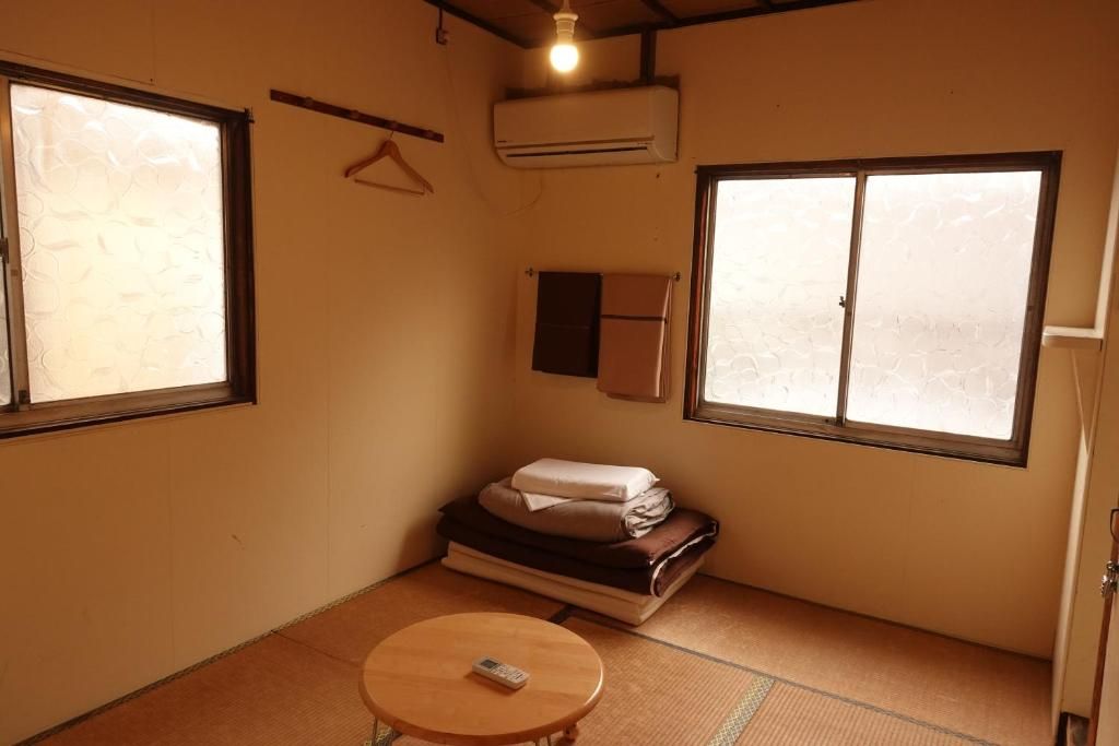Una habitación pequeña con suelo de tatami, una cama con manta, una mesita de noche con control remoto y una ventana con vistas.
