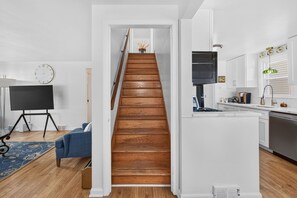 A staircase leading to a second floor, a kitchen with modern appliances, a flat-screen TV, and a clock on the wall. - Cozy Cape Cod House, centre of shopping & dinning (Buffalo)