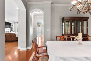 A dining area with a white table, wooden chairs, and a chandelier. - Whispering Pines Manor - Luxury Lake Retreat (Northport)