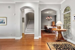 A spacious hallway with a staircase, a dining area with a chandelier, and a large window with a view. - Whispering Pines Manor - Luxury Lake Retreat (Northport)