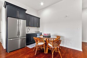 A compact kitchen with dark cabinets, a stainless steel refrigerator, a microwave, and a dining table with wicker chairs. - Whispering Pines Manor - Luxury Lake Retreat (Northport)