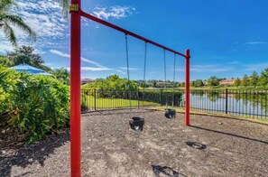 A playground with swings and a fenced area, near a body of water and greenery. - Minutes from Magic!!! (Kissimmee)
