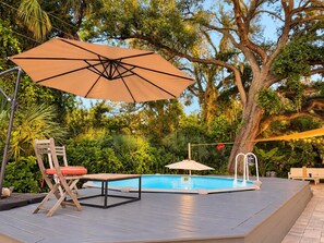 Un espace aménagé au bord de la piscine, avec une terrasse en bois, une chaise longue, une table et un parasol.