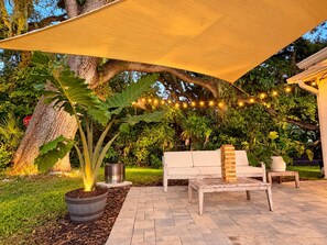 Un espace extérieur aménagé en terrasse, avec une table en bois, un canapé blanc et une grande plante en pot.