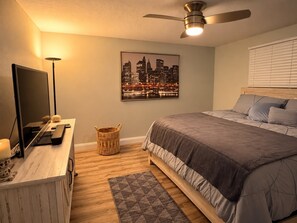 A bedroom with a bed, a television, a ceiling fan, a cityscape painting, and a wooden nightstand. - Enjoyable, tropical 3-bedroom house w/ pool and leisure areas in sunny Tampa Bay (Tampa)