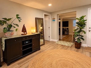 A well-lit living room with a dark wooden cabinet, a large woven rug, and potted plants. - Enjoyable, tropical 3-bedroom house w/ pool and leisure areas in sunny Tampa Bay (Tampa)