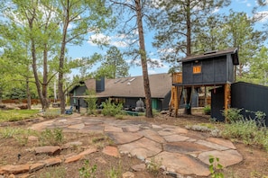 A cabin with a stone patio, surrounded by trees. - Mnt Elden Base Camp - 3BD/2BTH - Sleeps 8 - Trails (Flagstaff)