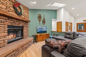Een woonkamer met een stenen openhaard, een ruime bank en een schilderij van een berglandschap.