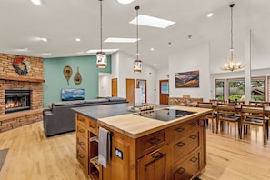 A spacious living area with a fireplace, a large island with wooden drawers, and a dining area with wooden furniture. - Mnt Elden Base Camp - 3BD/2BTH - Sleeps 8 - Trails (Flagstaff)