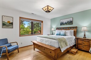 A bedroom with a bed, two bedside tables, a nightstand, a chair, and a window with a view of greenery. - Mnt Elden Base Camp - 3BD/2BTH - Sleeps 8 - Trails (Flagstaff)
