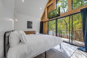 Un dormitorio con un ventanal grande, una cama con sábanas blancas, un cabecero de madera y una obra de arte colgada en la pared.