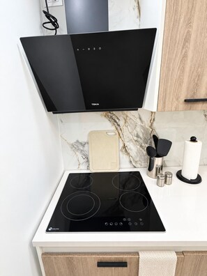 A kitchen with a black induction cooktop, a white countertop, and a marble backsplash.