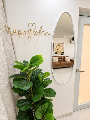 A hallway with a large mirror reflecting a living room, a potted plant, and a wall with a 'happy place' sign. - Carolina Luxe 2BR Escape Near SJU (Carolina)