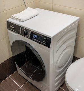 Eine kompakte, moderne Waschmaschine mit digitaler Anzeige neben einer Toilette in einem kleinen Badezimmer.