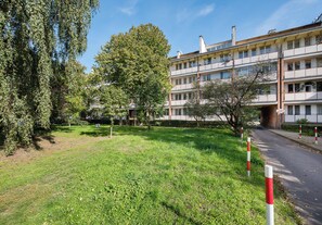 A residential building with multiple balconies, a grassy courtyard, and trees. - Park Moczydło Cozy Studio (Warszawa)
