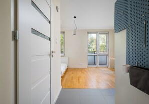 A modern interior with a wooden floor, a white door, and a view of a balcony with glass doors. - Park Moczydło Cozy Studio (Warszawa)