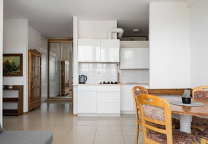 A modern kitchen with white cabinets, a dining table with chairs, and a small potted plant. - Ochota Standard Apartment (Warszawa)