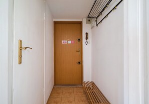 A narrow hallway with a wooden door, a metal intercom, and a small sign on the wall. - Ochota Standard Apartment (Warszawa)