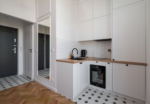A compact kitchen with white cabinetry, a black dishwasher, and a wooden countertop. - Ochota Studio with Mezzanine (Warszawa)