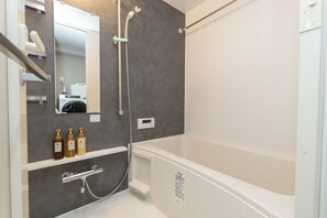 Et moderne badeværelse med badekar, bruser, indbygget vaskemaskine og et hylder med toiletartikler.