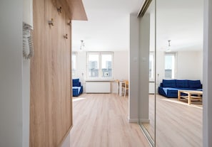 A modern apartment with a wooden floor, a blue sofa, a dining table, and a view of the city through large windows. - Ochota Green Spot Studio (Warszawa)