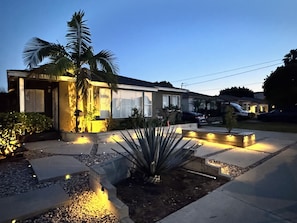 A residential house with a well-lit driveway, palm trees, and a clear sky. - Charming bedroom in private home (Hawthorne)