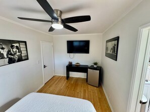 A bedroom with a bed, a ceiling fan, a desk with a television, and two framed pictures on the wall. - Charming bedroom in private home (Hawthorne)