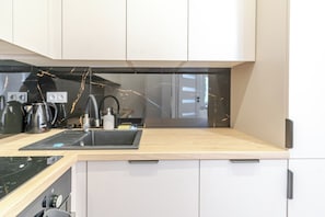 A modern kitchen with a black countertop, white cabinets, and a stainless steel sink. - Urban Nest Modern Studio (Katowice)