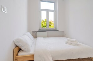 A single-bed room with a window, white bedding, and a radiator. - Urban Nest Modern Studio (Katowice)