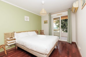 A bedroom with a bed, bedside table, lamp, and a view of the outside. - Upstays Spacious 2BR 100m² with terrace and pool (Cannes)