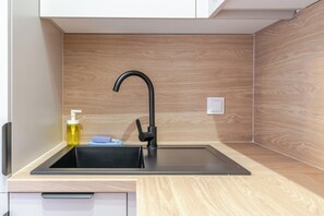 A compact kitchen with a modern black faucet, a small soap dispenser, and a bottle of liquid soap on the counter. - Urban Nest Chic Studio (Katowice)