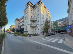 A multi-story building with a central courtyard, a pedestrian crossing, and a street with cars and a pedestrian. - Urban Nest Chic Studio (Katowice)