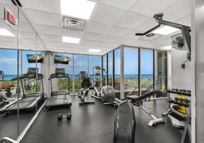 Une salle de sport équipée de tapis de course, d’un appareil elliptique et de poids libres, avec une vue sur l’océan grâce à de grandes fenêtres.