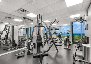 Ein Fitnessstudio mit unterschiedlichen Trainingsgeräten, großen Spiegeln und Meerblick durch die Fenster.