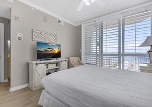 Ein Schlafzimmer mit Bett, Fernseher, Schreibtisch und einem Fenster mit Jalousien.