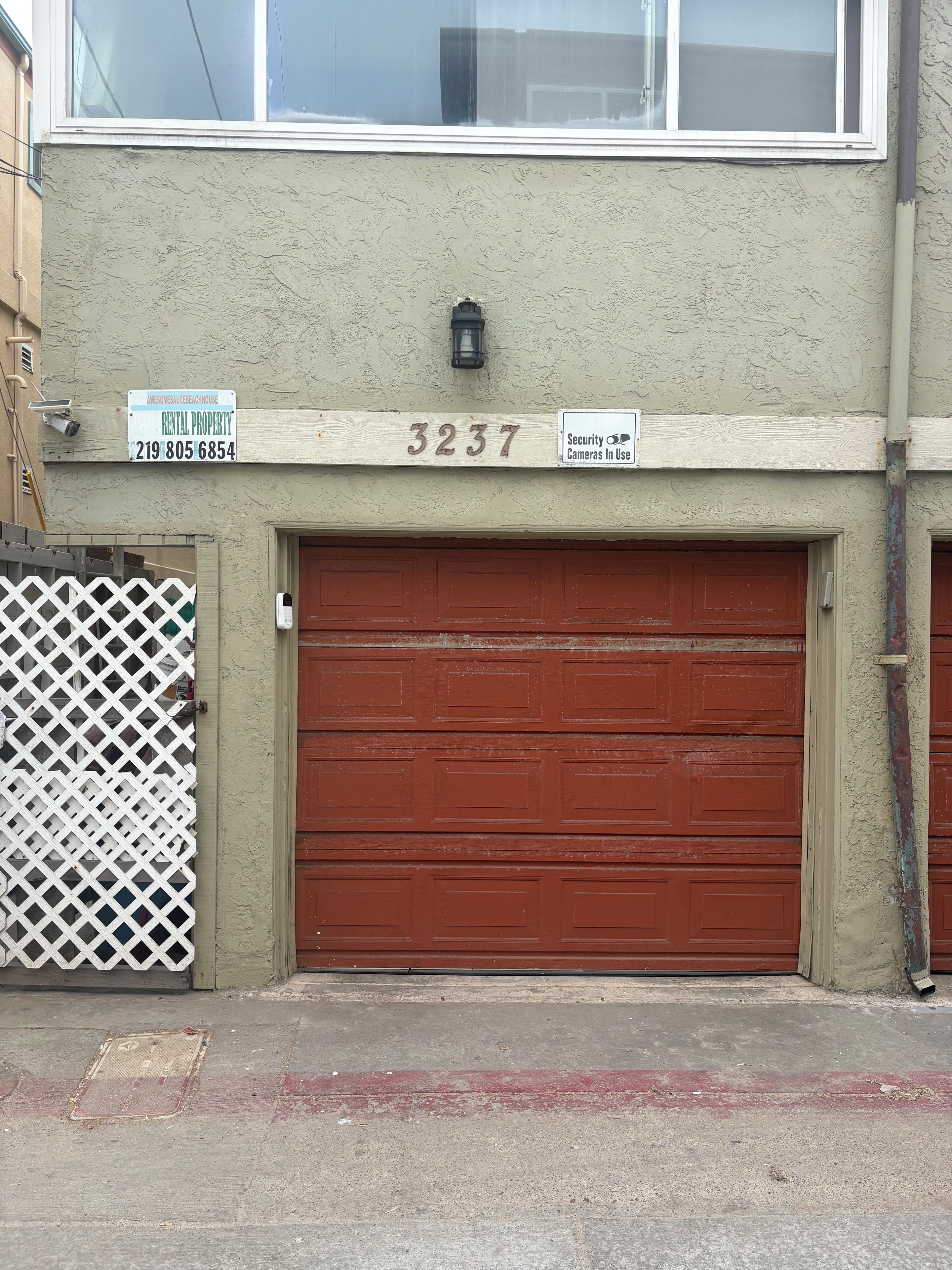 Un edificio con puerta de garaje roja, cámara de seguridad y un cartel que indica que es una propiedad de alquiler.
