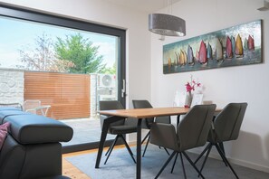 Ein zeitgemäßer Essbereich mit Holztisch und -stühlen, einem Segelbootgemälde an der Wand und Blick ins Freie durch eine Glastür.