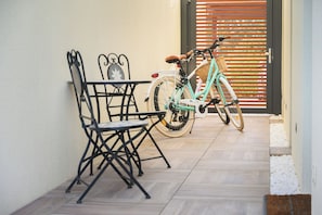Un espace patio comprenant une table et des chaises, un vélo et une porte en bois avec des stores.