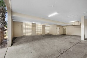 Ett rent, tomt parkeringsgarage med betonggolv och -väggar, stora fönster med persienner och en palm utanför.