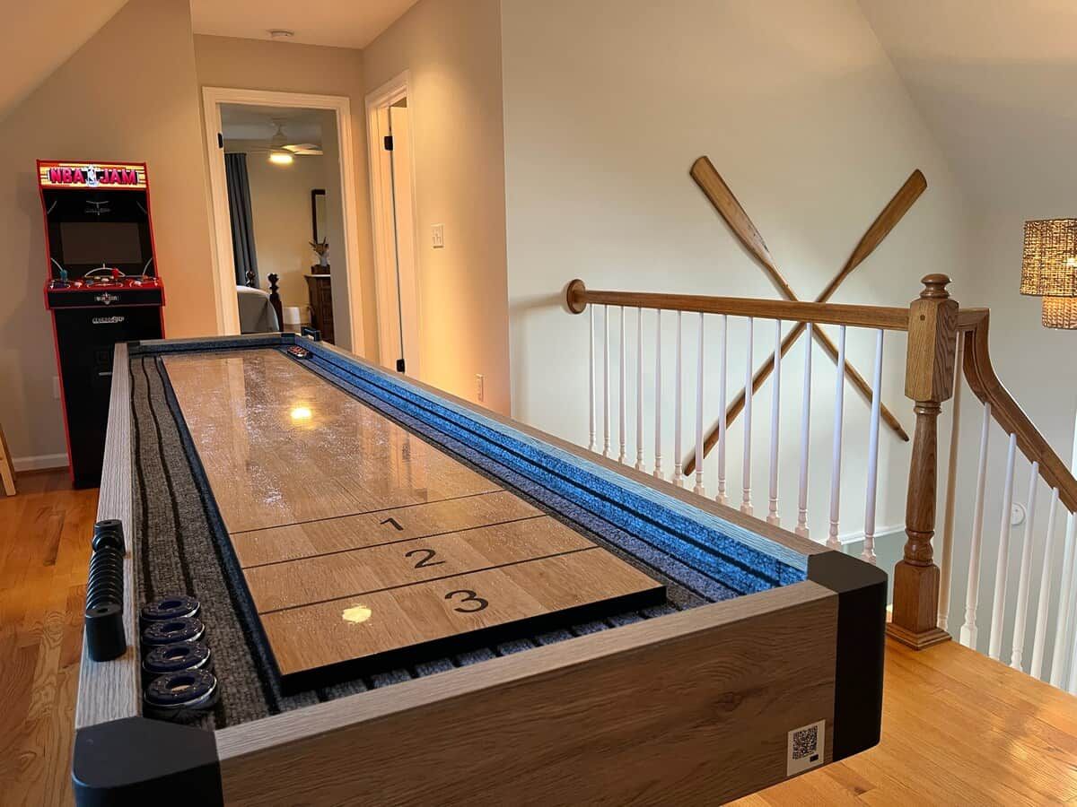 A shuffleboard table with numbered ends, a wooden railing, and a door in the background.
