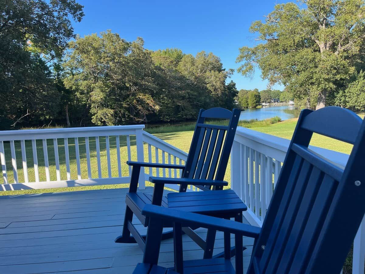 A deck with two Adirondack chairs and a white railing overlooking a lake.