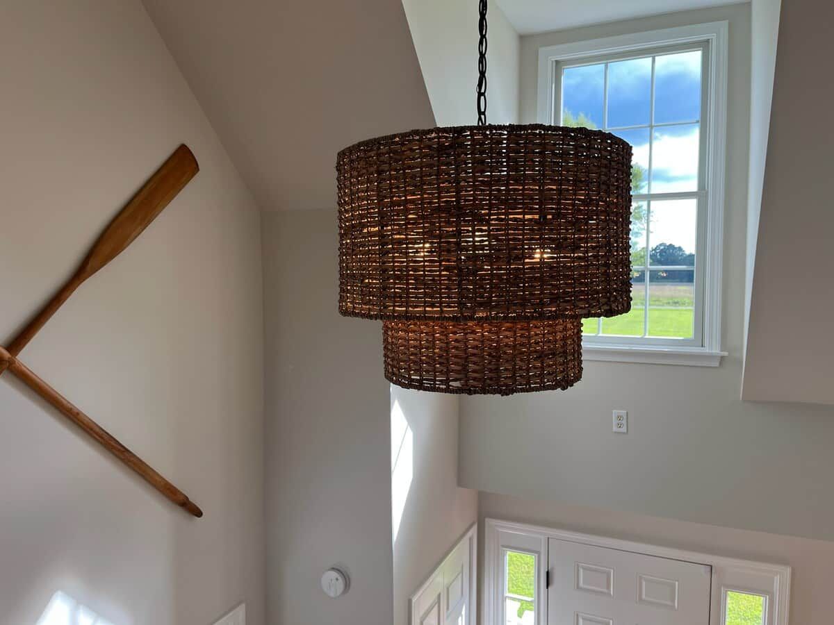 A room with a woven pendant light fixture, a wooden bat leaning against the wall, and a view of a green landscape through a window.