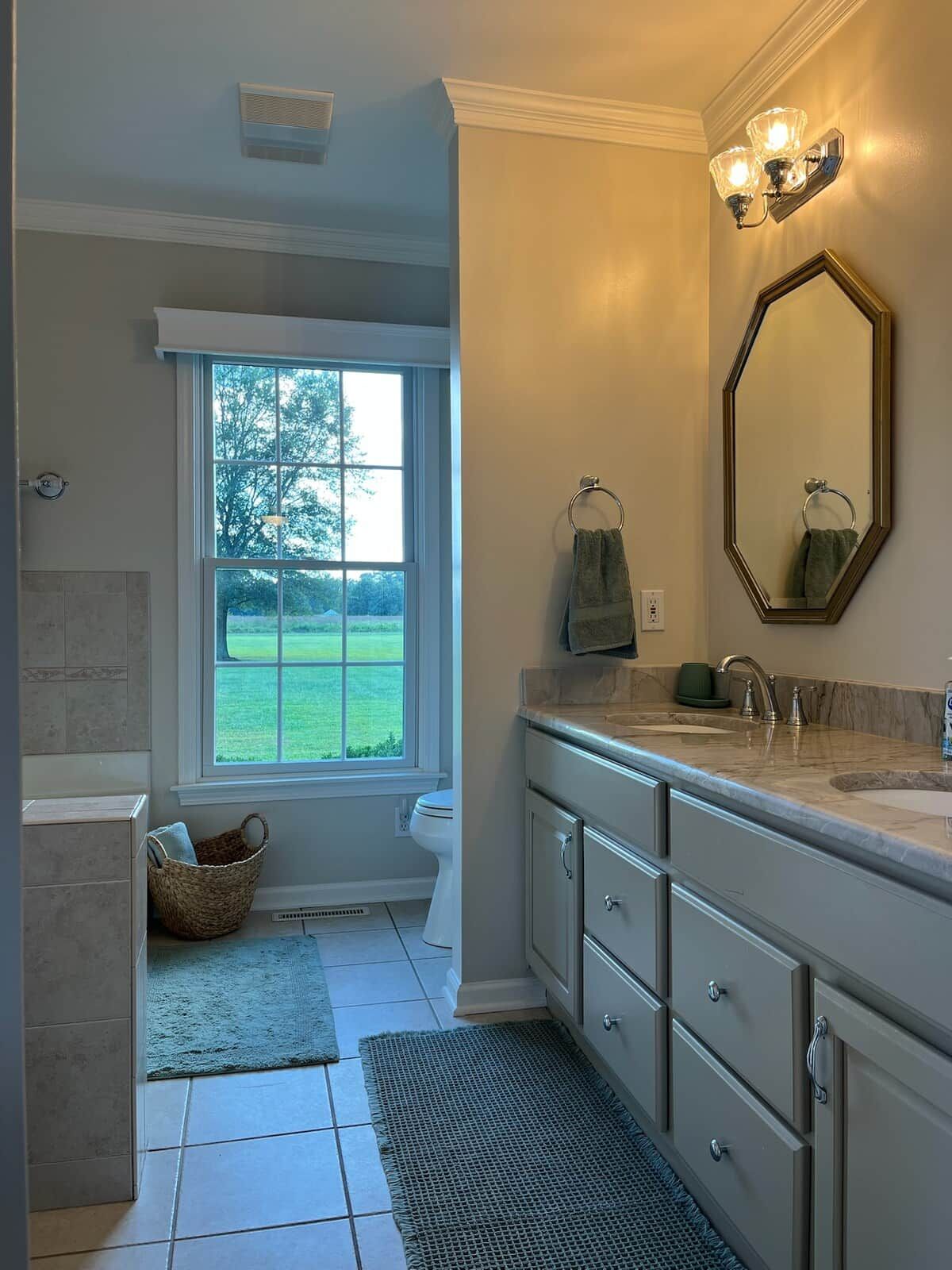 A bathroom with a large window, a bathtub, a vanity with a mirror, and a towel rack.