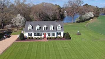 A two-story house with a front porch, a lawn, and a body of water in the background.