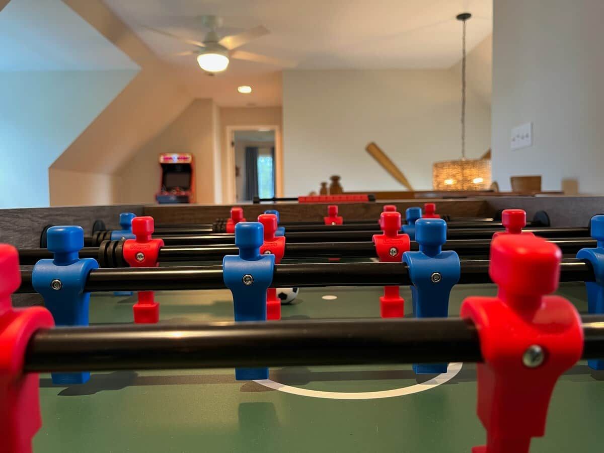 A foosball table in a room with a ceiling fan, a door in the background, and a hanging light fixture.