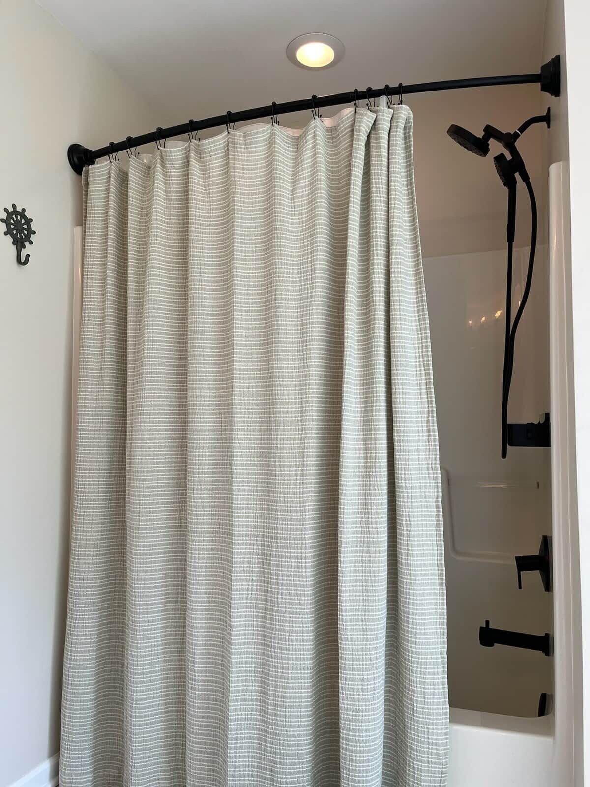 A bathroom with a shower curtain, a wall-mounted light fixture, and a black towel rack.