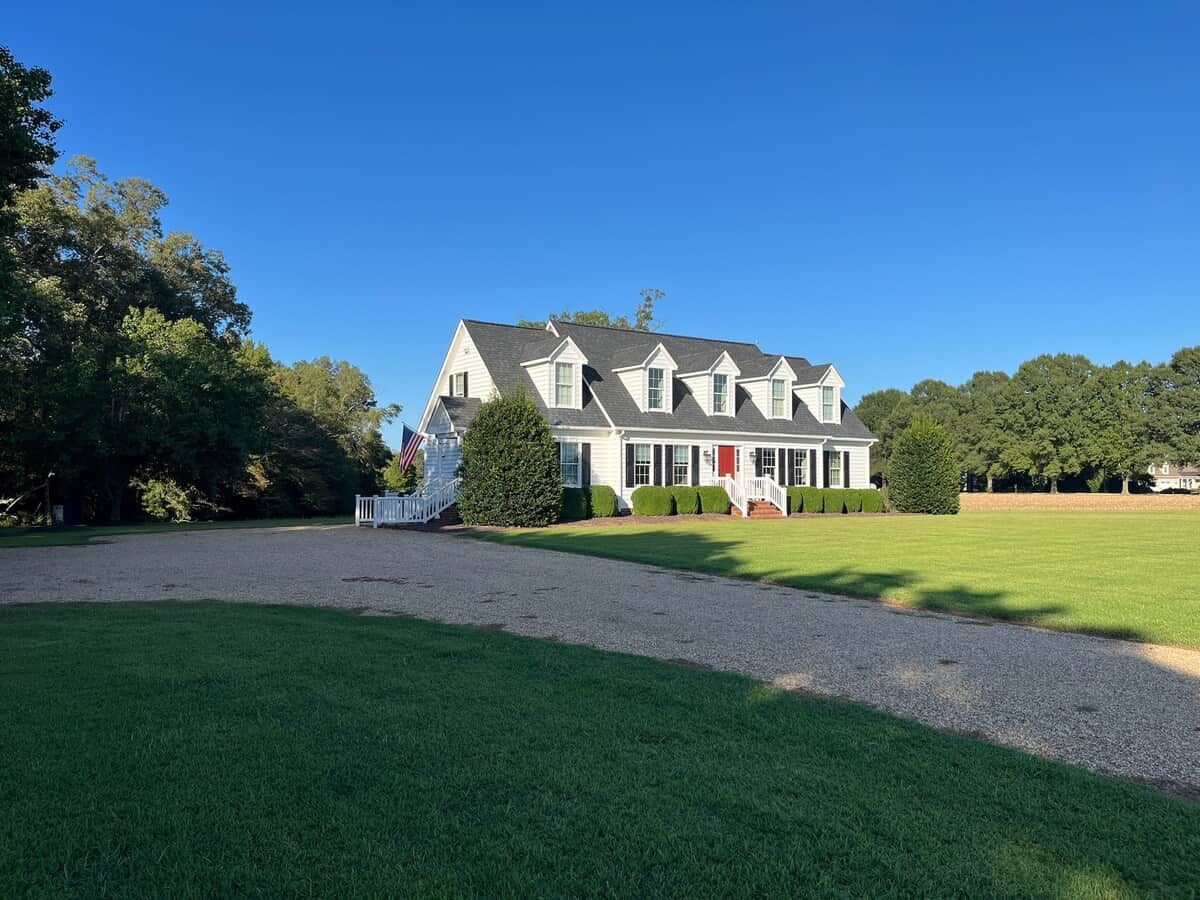 A large, multi-story house with a front porch, surrounded by a well-maintained lawn and trees.