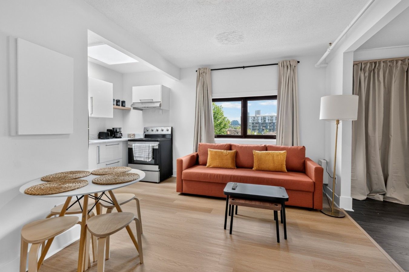 A modern living space with a kitchen, a sofa, a dining area, and a view of the city.