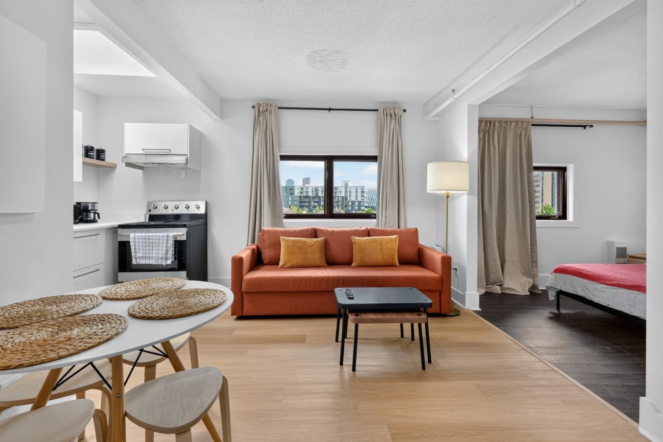 A modern apartment with a kitchen, a living area with a sofa and a dining table, and a bedroom with a bed.